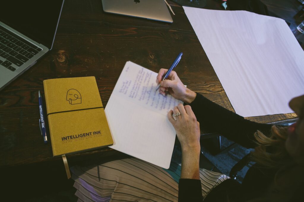 Image of someone drafting ideas/ writing their book by hand, with an Intelligent Ink notebook next to them.