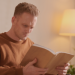 Image of a white man reading a book and looking unhappy or confused
